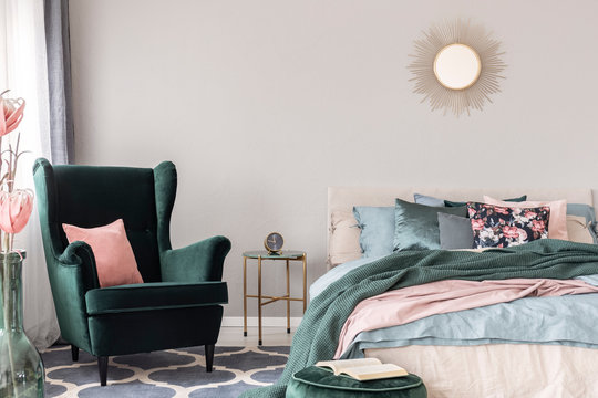 Emerald Green Armchair With Pastel Pink Pillow Next To Stylish Nightstand Table With Clock In Fashionable Bedroom Interior