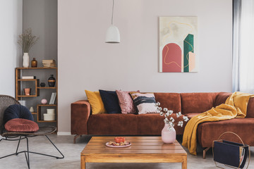 Flowers in vase on wooden coffee table in fashionable living room interior with brown corner sofa with pillows and abstract painting on the wall - obrazy, fototapety, plakaty
