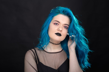 people, fashion and hair concept - close-up portrait of young woman in black dress with blue hair on black background