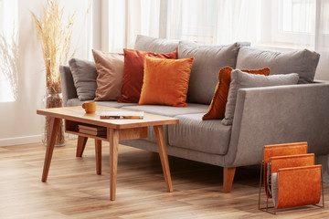 Living room with wooden coffee table and grey couch with ginger, orange and red pillows