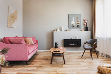 Stylish living room interior with pastel pink sofa, wooden coffee table and eco fireplace