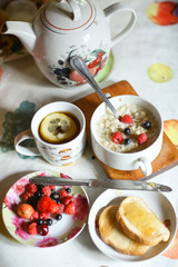 breakfast still life with oatmeal, seasonal berries, roasted toasts with lemon jam cup of tea spoon and knife
