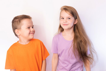 Little cute boy and girl in bright t-shirts, smiling on light background