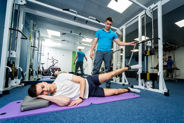 Fototapeta na wymiar Rehabilitation therapy. Young man doing exercises on mat under supervision of physiotherapist.