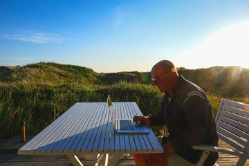 Hirtshals Denmark A man working on a computer on the patio at sunset.