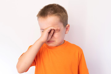 Cute little boy with tear-stained face and hand wipes his tears on a light background