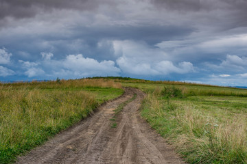 Obraz premium Dirt road leading to the top of the hill, dramatic storm clouds at summertime in Transylvania, Romania.