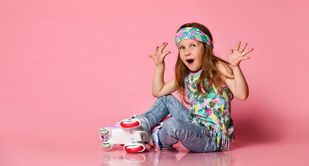 Little baby blond hair child sitting with roller skates in a white shirt and hairband happy smile...