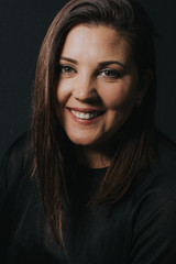 Low key studio portrait of women in her thirties smiling to camera.
