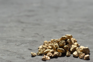 Golden sones. A pile of Gold nugget grains, on gray cement background, copy space