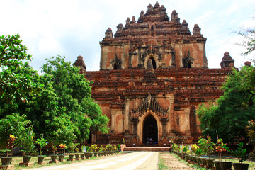Fototapeta premium Straight path between trees, leading to an old and big buddhist temple out of bricks in Bagan, Myanmar/Birma.