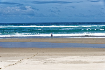 Fototapeta na wymiar Frau blickt hinaus auf das stürmische Meer ein Fusspur im Sand führt zu ihr.