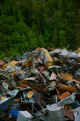 Large junk pile outside of town with trees and hilly background
