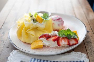 Crepe and ice cream with fresh fruit on wooden table.