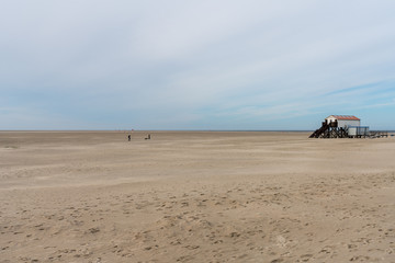 Fototapeta na wymiar Langer Sandstrand am Meer mit Gebäude und Fußgänger am Horizont