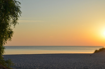 Fototapeta na wymiar Sunset by a beautiful empty sand beach