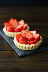 Tartlets with custard and fresh strawberries served on a slate plate