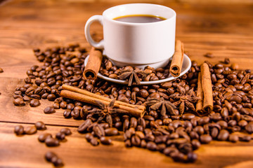 Cup of hot coffee, star anise, cinnamon sticks and scattered coffee beans on wooden table