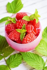 Fresh,ripe raspberries in a Cup and green raspberry leaves on a white background.