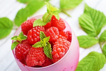 Fresh,ripe raspberries in a Cup and green raspberry leaves on a white background.