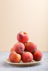 Fresh peaches on a plate on gray and orange pastel background. side view.