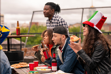 Young multicultural football fans in casualwear having pizza and beer