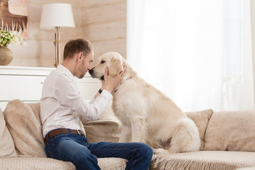 Young handsome guy teaches his big dog to the rules sitting on the sofa in the living room of his country house. Dog training concept