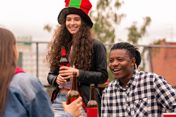 Young intercultural couple of soccer fans having beer while chatting with friend