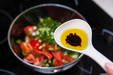 Preparation of salad from fresh vegetables, cucumbers, tomatoes and greens with a white plastic spoon containing a salad dressing made from olive oil, balsamic vinegar and soy bean sauce