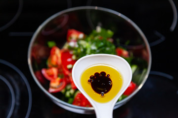 Preparation of salad from fresh vegetables, cucumbers, tomatoes and greens with a white plastic spoon containing a salad dressing made from olive oil, balsamic vinegar and soy bean sauce