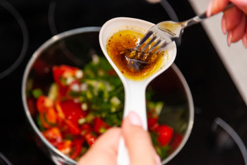 Preparing a salad of fresh vegetables, cucumbers, tomatoes and greens with a white plastic spoon in which the dressing of olive oil, balsamic vinegar and soy bean sauce is mixed with a fork