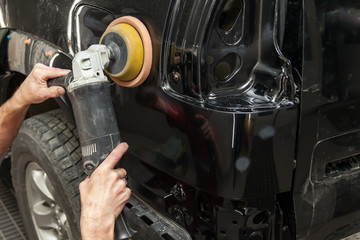 Close-up view on the hands of a male worker who holds a tool for polishing the fender of a car...