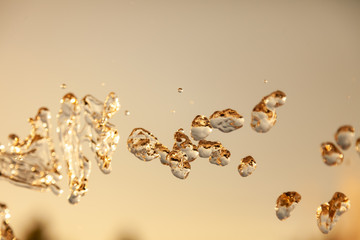 Water droplets frozen in the air with splashes and chain bubbles on a golden and bronze isolated...
