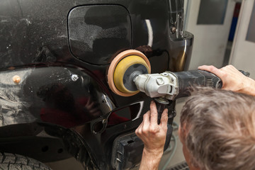 Close-up view on the hands of a male worker who holds a tool for polishing the fender of a car...