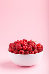 Fresh raspberry in white bowl on pink pastel background. side view.