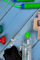 Sports equipment for fitness training on a wooden background. Bottle with water, smart watch, earphones and jumping-rope. Set for sports activities.