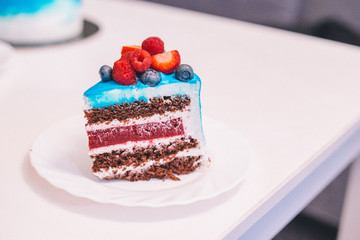 Close-up of a piece of festive blue and white cake decorated with fruits: strawberries, raspberries, blueberries. Cake for birthday, holiday and anniversary. Cake slice with filling