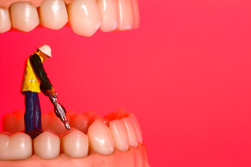 Miniature figure workman with a road drill amongst a pair of false teeth toothache and filling...