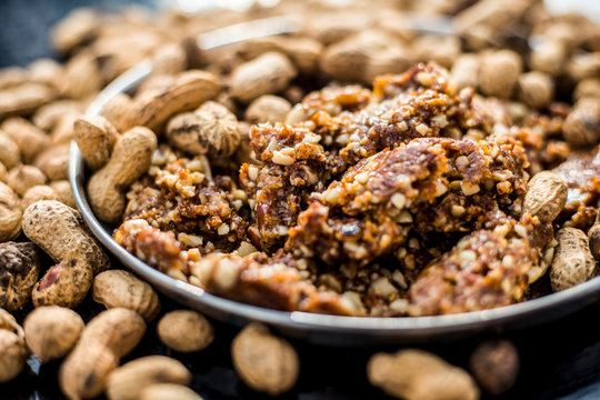 Mandvi pak, sing pak, chiki, peanut barfi or chikki in a silver colored plate along with roasted peanuts and some raw also on the wooden surface.