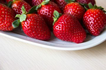 Fresh strawberries on a white plate on a wooden light background, copy space. Strawberry background. Sweet, juicy, ripe strawberries. Harvest of organic local  strawberries. Healthy food with vitamins