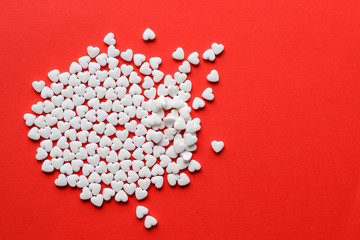White pills in the shape of a heart on a red background.