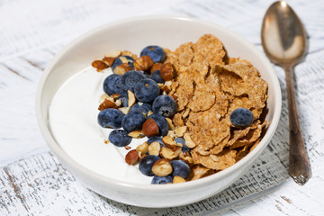 bowl of healthy wholegrain flakes, yogurt and blueberries on white table