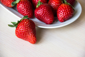 Fresh strawberries on a white plate on a wooden light background, copy space. Strawberry background. Sweet, juicy, ripe strawberries. Harvest of organic local  strawberries. Healthy food with vitamins