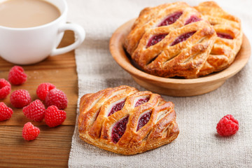 puff pastry buns with strawberry jam on wooden background with linen textile and a cup of coffee. side view.