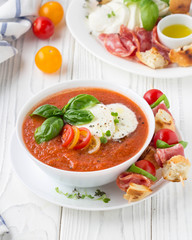 Tomato cold gazpacho soup with vegetables, mozzarella, salami, croutons and basil. Traditional Spanish summer food