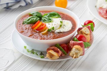 Tomato cold gazpacho soup with vegetables, mozzarella, salami, croutons and basil. Traditional Spanish summer food