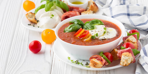 Tomato cold gazpacho soup with vegetables, mozzarella, salami, croutons and basil. Traditional Spanish summer food