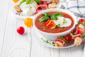 Tomato cold gazpacho soup with vegetables, mozzarella, salami, croutons and basil. Traditional Spanish summer food