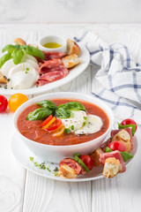 Tomato cold gazpacho soup with vegetables, mozzarella, salami, croutons and basil. Traditional Spanish summer food