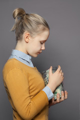 Pretty girl teen and money in glass jar on gray background